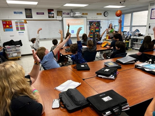 Kids in classroom raising hands during health program