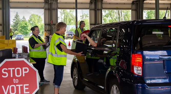 A KREMC employee stands by a car holding a ballot box while a member slips their ballot into the box.