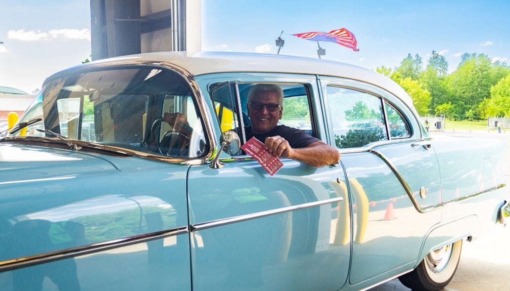 A KREMC member in a classic car holds his voting ballot out of his window.