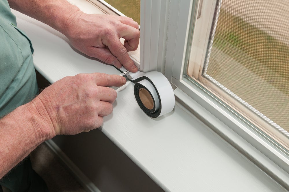 A man applies weather stripping to a window.