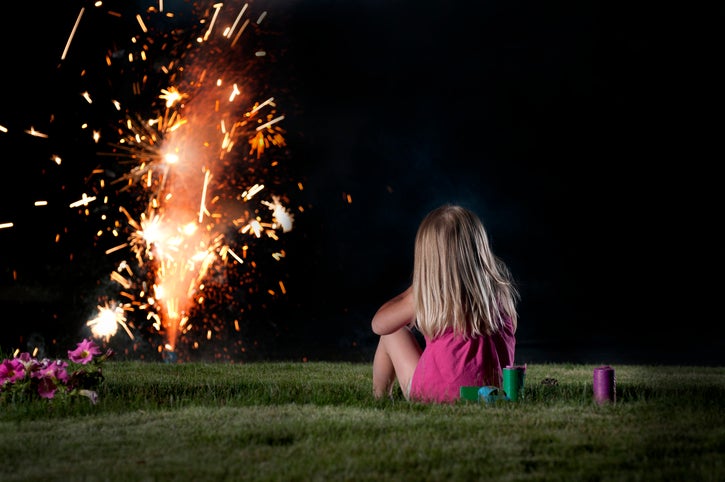 A child sits and watches a fireworks display from a safe distance. 