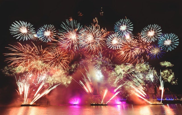 An elaborate fireworks display erupts from a shimmering lake and fills the night sky.